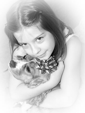 Black and white photo of a young girl cuddling her puppy, who is wearing a rosette.