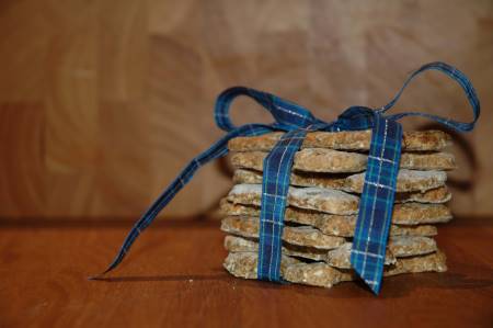 A stack of peanut butter dog treat recipes, tied up on a blue and gold ribbon, placed on a wooden board.